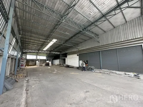 Warehouse for sale in Bang Khen, Bangkok - Spacious warehouse interior with steel trusses, skylight panels and multiple roller doors.