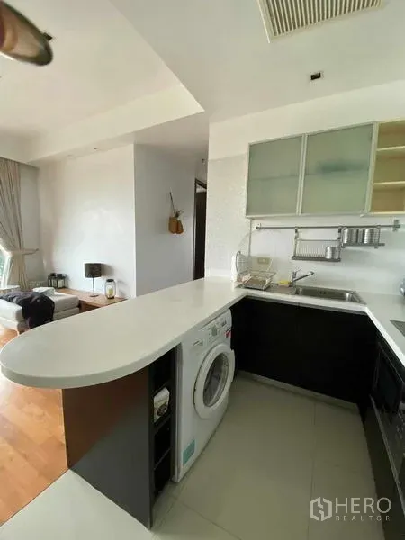 Condominium for rent in Yan Nawa, Bangkok - Modern U-shaped kitchen with white breakfast bar, built-in washer, and open-plan layout beside the living area.