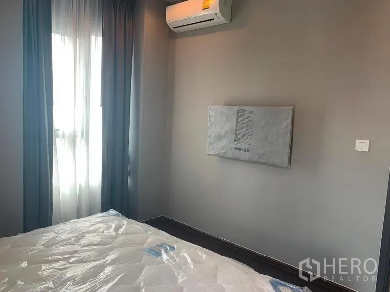 Condominium for rent in Watthana, Bangkok - Second bedroom with air conditioner, wall-mounted TV point and curtained window.