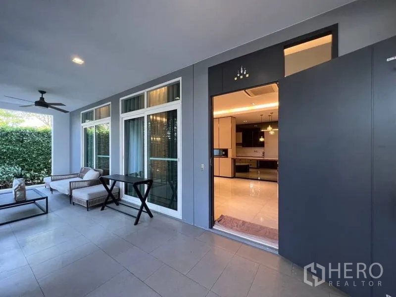 Detached House for rent or sale in Bang Phli, Samut Prakan - Shaded terrace with ceiling fan, lounge seating and sliding glass doors opening to the kitchen.