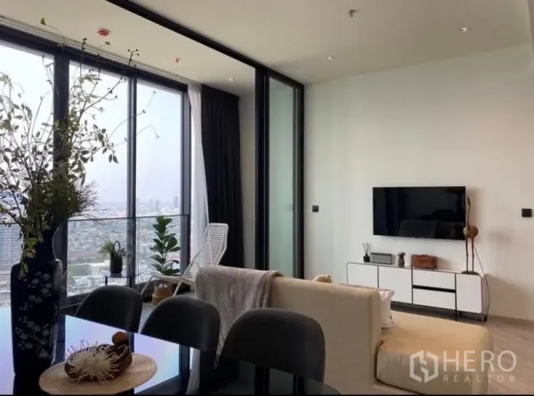 คอนโด ให้เช่า - ห้องนั่งเล่นสว่างพร้อมกระจกเต็มผนัง ทีวีติดผนัง และวิวเมืองแม่น้ำ