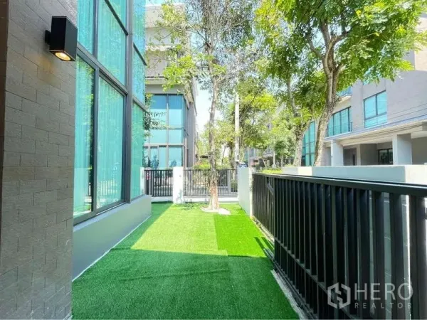 Detached House for rent in Bang Sue, Bangkok - Private side garden with artificial turf, trees and a black metal fence.