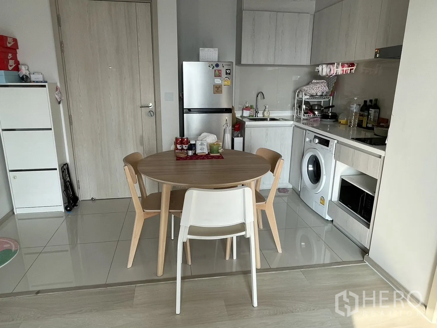 Condominium for rent in Pathum Wan, Bangkok - Kitchen and dining space with round wooden table, fridge and white cabinets with integrated washer.
