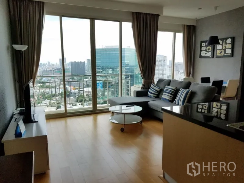 Condominium for rent in Chatuchak, Bangkok - Open‑plan lounge and kitchen with floor‑to‑ceiling windows framing the Bangkok skyline.