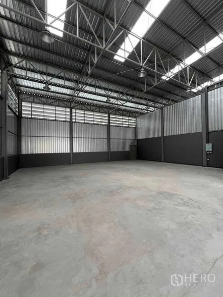 Warehouse for rent in Phra Samut Chedi, Samut Prakan - Spacious warehouse interior showing steel truss roof, skylight panels, and smooth concrete floor.