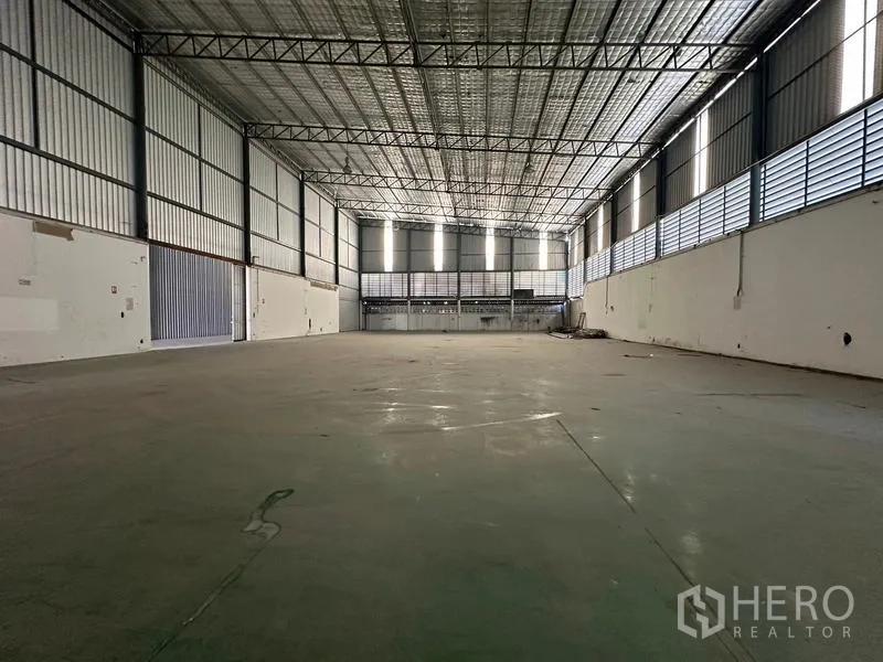 Warehouse for rent in Suan Luang, Bangkok - Open industrial floor with steel truss roof, ventilation louvers and bright skylights.