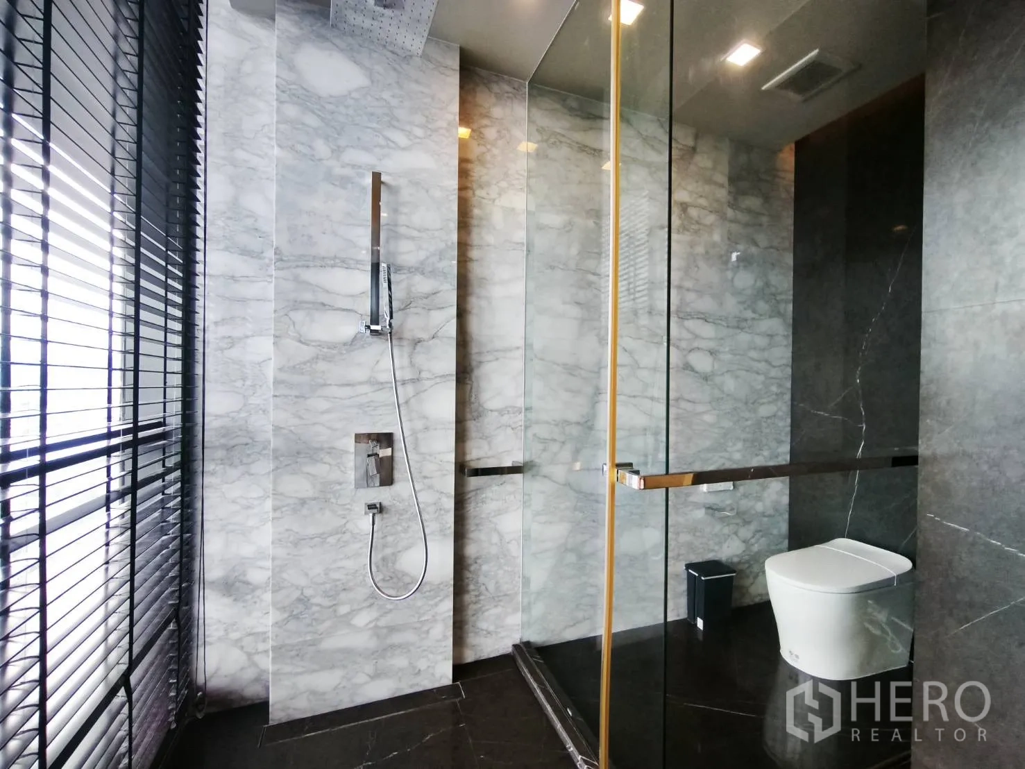 Condominium for rent in Watthana, Bangkok - Marble-clad bathroom with rain shower, glass partition, and toilet.