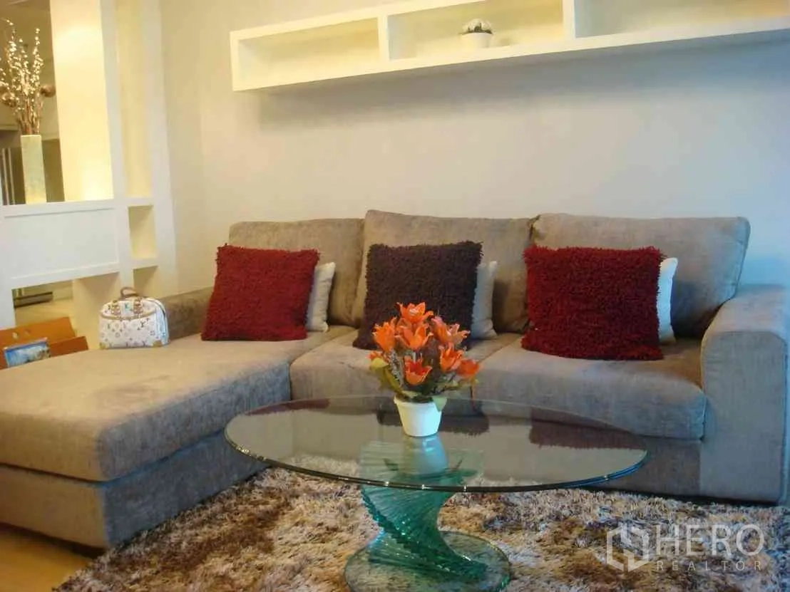 Condominium for rent in Watthana, Bangkok - Bright living room with gray L-shaped sofa, glass coffee table and floating shelves in a modern Sukhumvit condo.