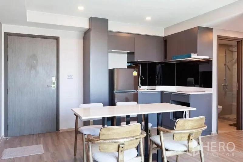 Condominium for rent or sale in Watthana, Bangkok - Open-plan kitchen and dining area with grey cabinetry, refrigerator and a four-seat table.