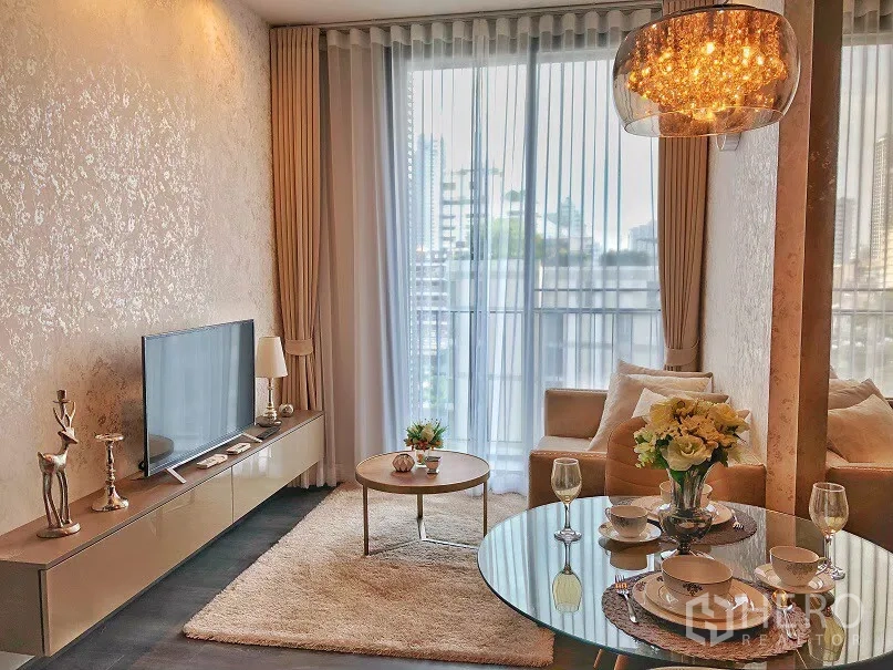 คอนโด ให้เช่าในWatthana, Bangkok - ห้องนั่งเล่นคอนโดในวัฒนา กรุงเทพฯ โทนอบอุ่น มีชั้นวางทีวี โต๊ะทานอาหารทรงกลม โคมไฟ และหน้าต่างเต็มบานเปิดสู่ระเบียงวิวเมือง