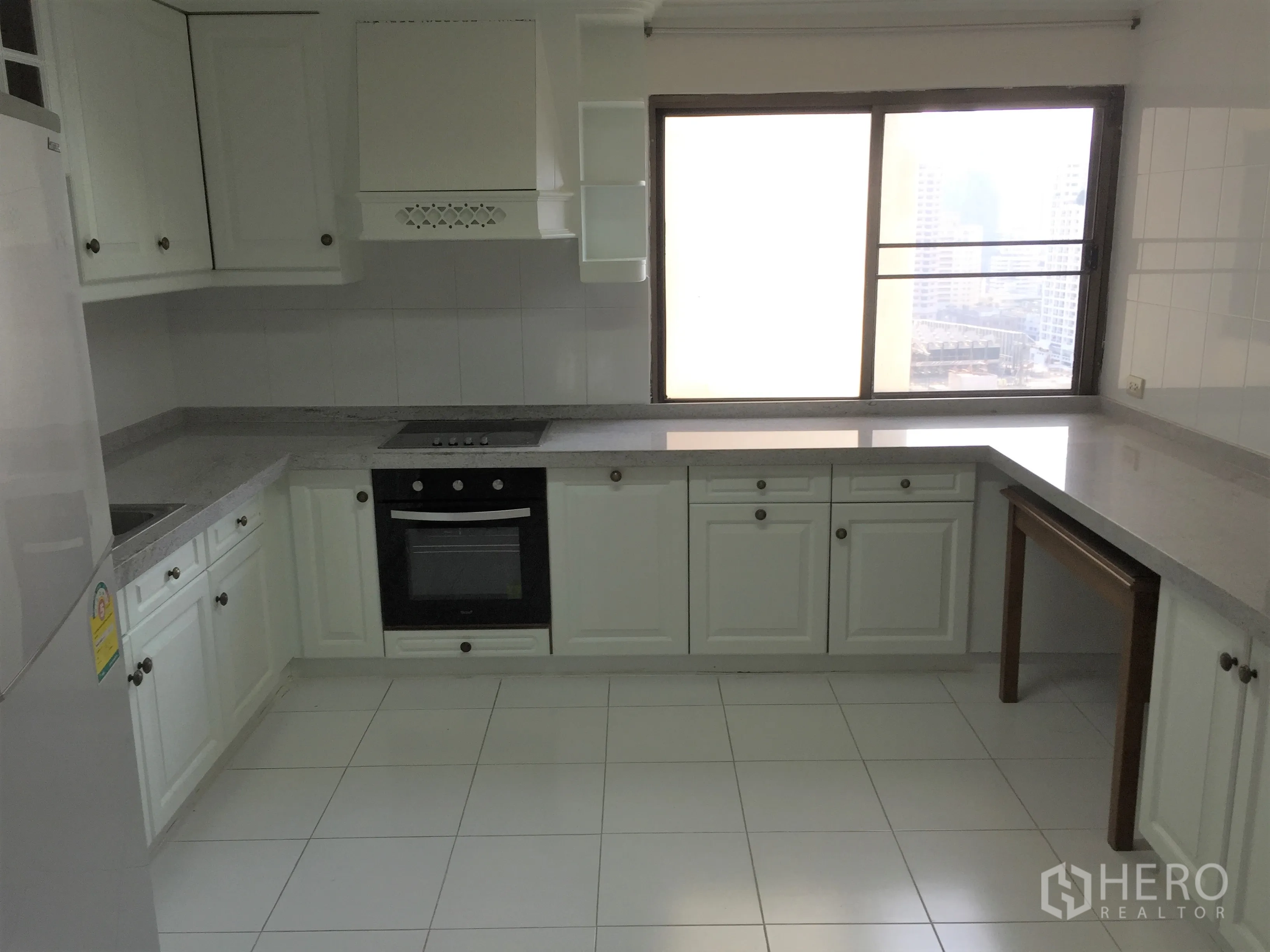 Condominium for rent in Watthana, Bangkok - Large U-shaped white kitchen with oven, cooktop, plenty of cabinets and a city-view window.