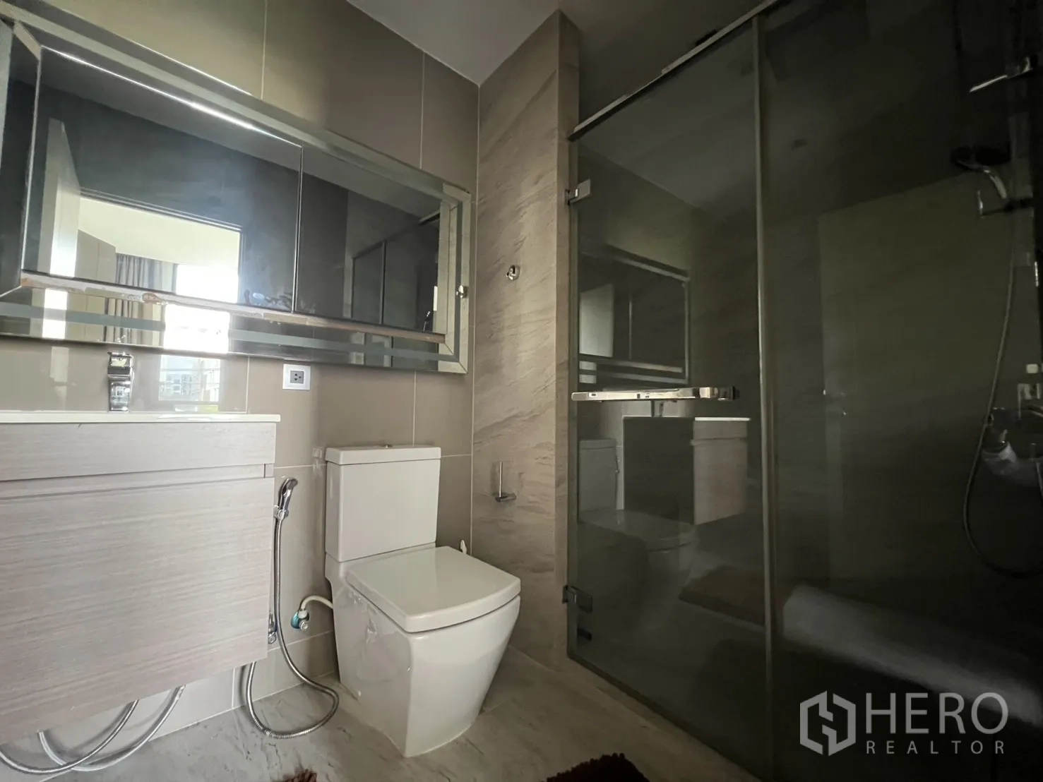 Condominium for rent in Watthana, Bangkok - Modern bathroom with vanity, toilet, and a glass-enclosed shower area.