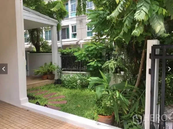 Townhouse for rent or sale in Suan Luang, Bangkok - Private front garden with stepping stones, lush plants, and a covered terrace inside a gated fence.