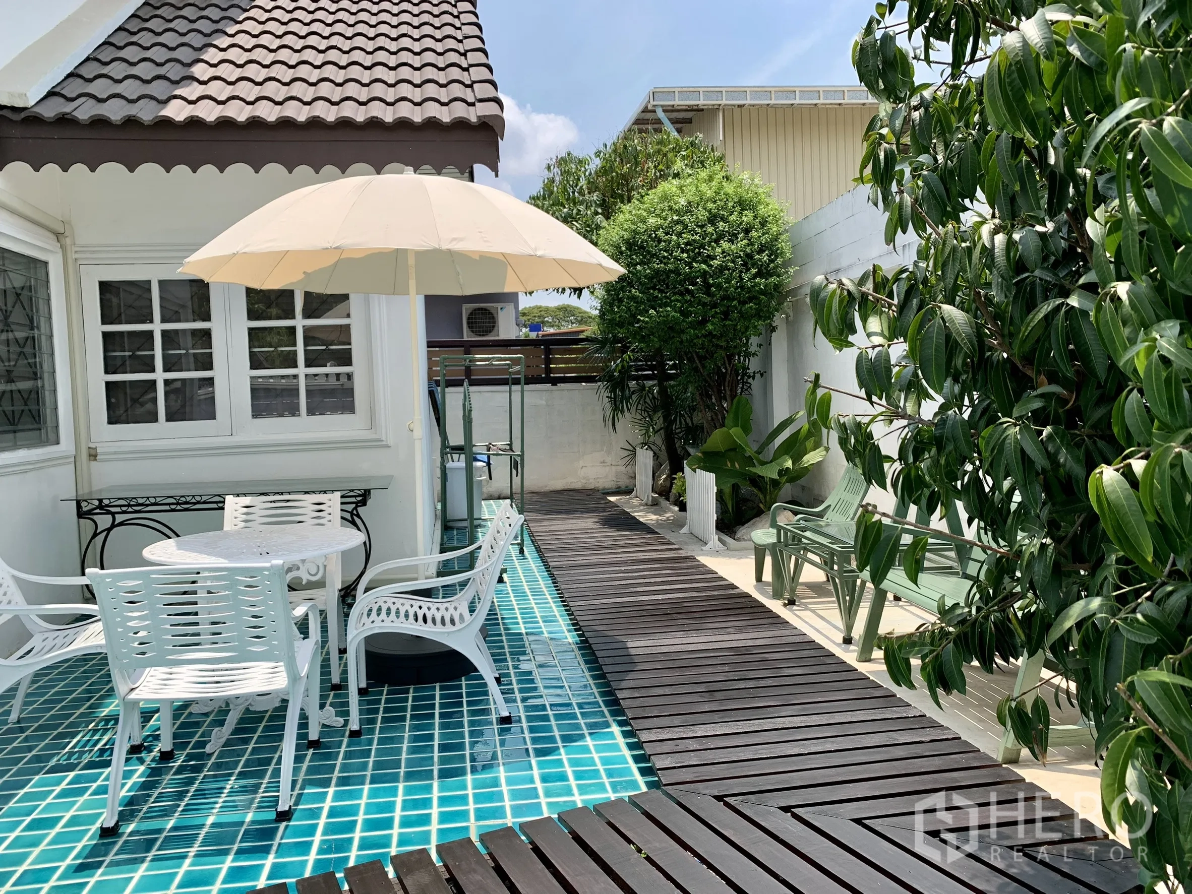 บ้านเดี่ยว for rent in Saphan Sung, Bangkok - เด็คไม้อยู่เหนือเฉลียงกระเบื้องสีฟ้า พร้อมโต๊ะกลม เก้าอี้ ร่ม และต้นไม้.