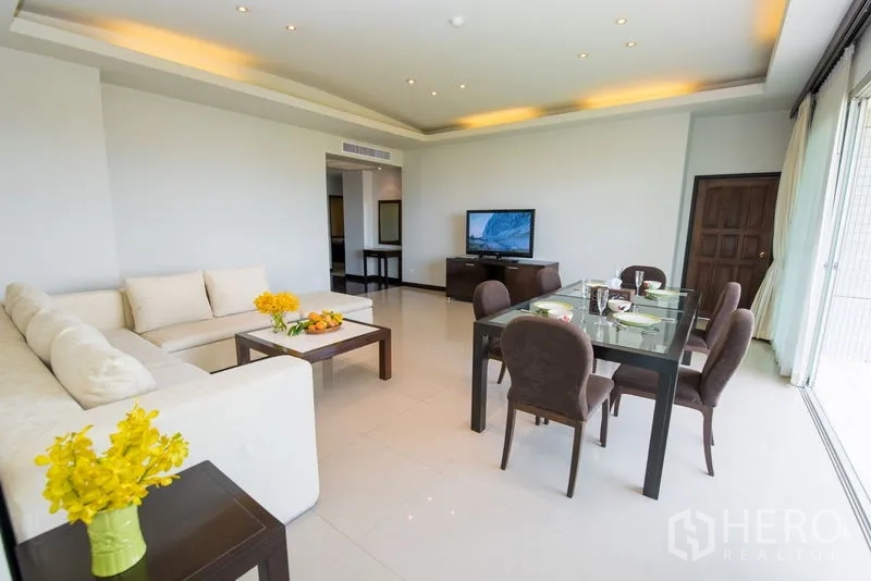 Condominium for rent in Sathon, Bangkok - Living room with TV console, sectional sofa and full-height sliding doors to the balcony.