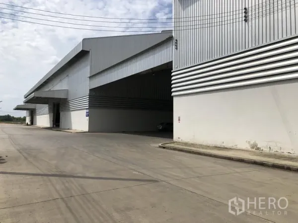 工厂 出租在Wang Noi, Phra Nakhon Si Ayutthaya - 大型仓库转角视角，宽大雨棚与笔直混凝土道路相连。