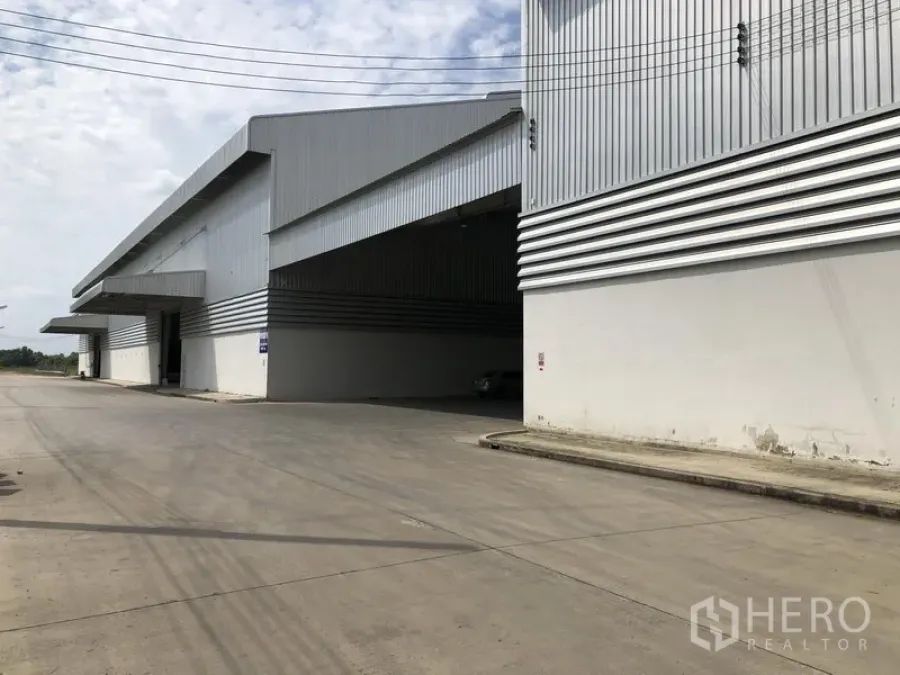 工厂 出租在Wang Noi, Phra Nakhon Si Ayutthaya - 大型仓库转角视角，宽大雨棚与笔直混凝土道路相连。