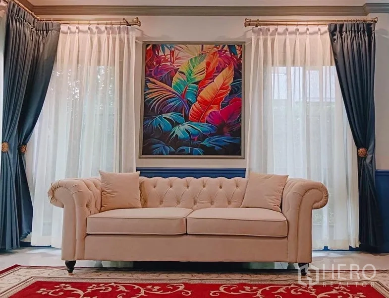 Detached House for rent or sale in Saphan Sung, Bangkok - Bright living room with beige tufted sofa, sheer curtains and colorful tropical artwork.