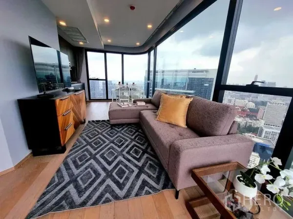 公寓 出租在Bang Rak, Bangkok - 转角客厅配L形沙发与电视柜，落地窗俯瞰曼谷天际线。