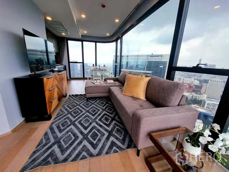 公寓 出租在Bang Rak, Bangkok - 转角客厅配L形沙发与电视柜，落地窗俯瞰曼谷天际线。