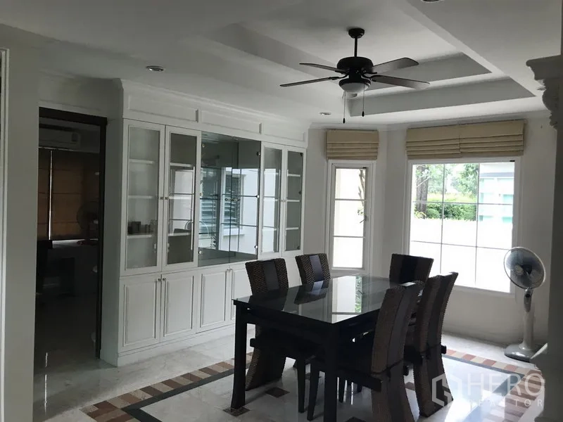 独立式住宅 出租在Phra Khanong, Bangkok - 餐厅配玻璃餐桌、大窗户、吊扇及内置展示柜。