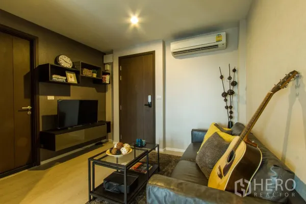 Condominium for rent or sale in Sathon, Bangkok - Cozy living room at Rhythm Sathorn-Narathiwas with grey sofa, guitar, floating TV unit and wall shelves.
