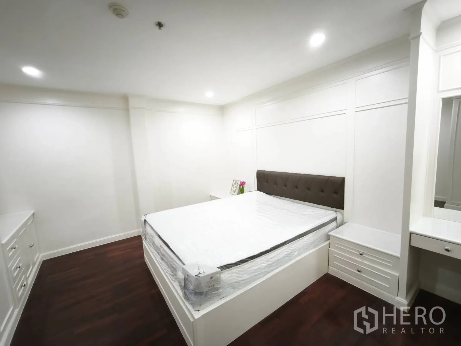 Condominium for rent in Watthana, Bangkok - Second bedroom with bed, bedside tables, white built-ins, and dark wood flooring.