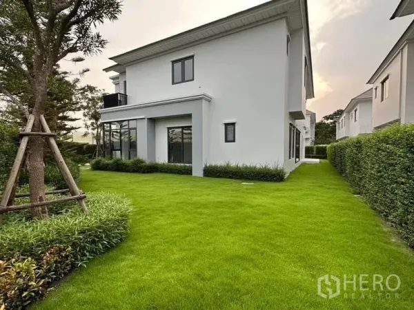 บ้าน ขายในLat Krabang, Bangkok - บ้านเดี่ยวสองชั้นสีขาวพร้อมสนามหญ้ากว้างและแนวรั้วต้นไม้