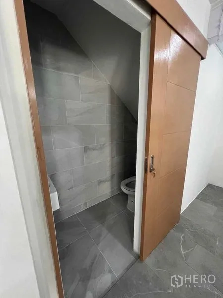 Townhouse for rent in Khlong Toei, Bangkok - Under‑stair toilet with sliding wooden door and tiled walls.