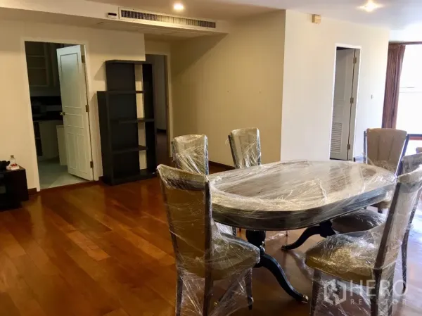 Condominium for rent or sale in Watthana, Bangkok - Dining area with wrapped table and chairs on polished wood floor, open to hallway.