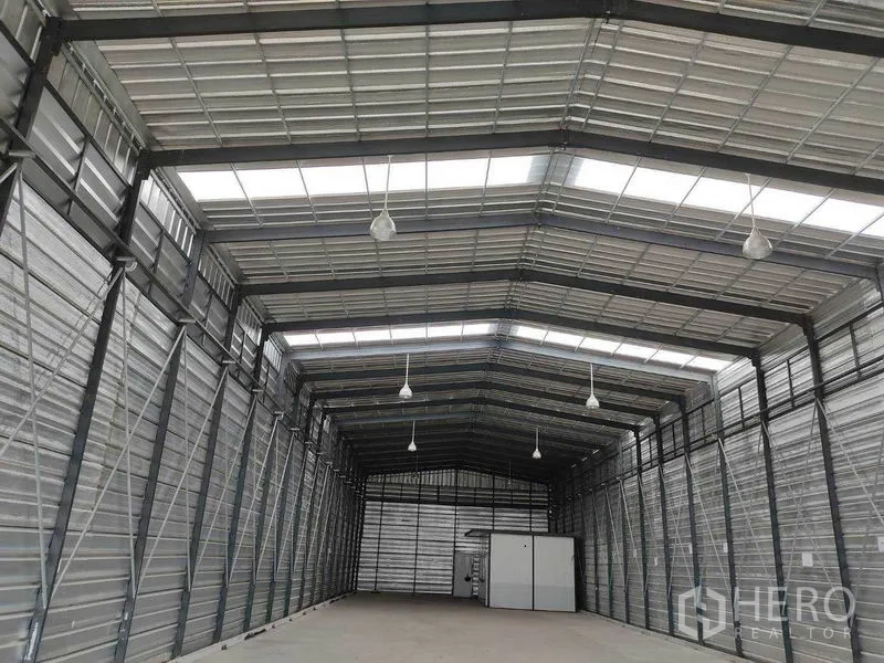 Warehouse for rent in Bang Phli, Samut Prakan - Steel truss roof with translucent skylight panels and hanging lights spanning the warehouse.