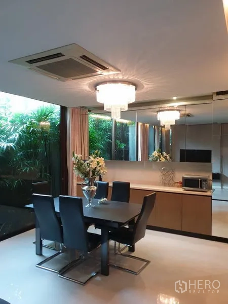 Detached House for sale in Watthana, Bangkok - Dining area with crystal chandelier, mirror wall and garden view.