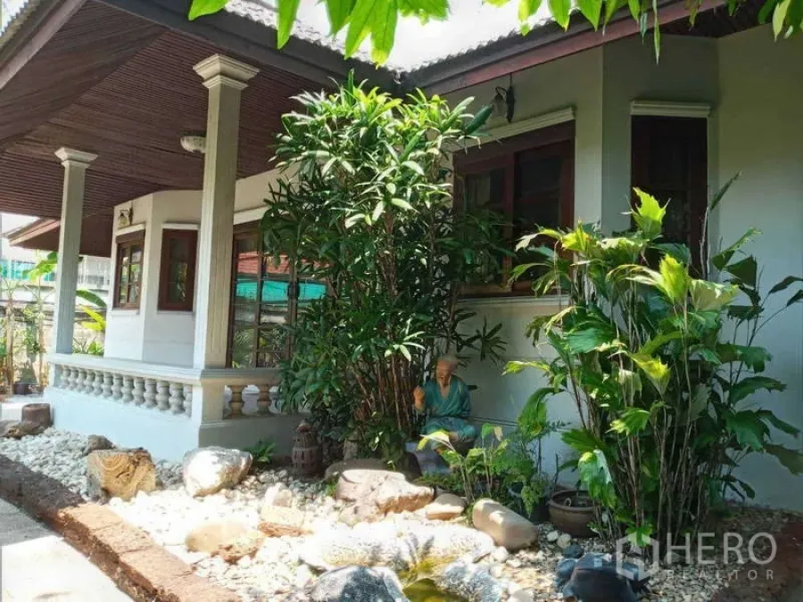 Detached House for rent in Khlong Toei, Bangkok - Corner exterior view of the house surrounded by dense greenery and stone landscaping.