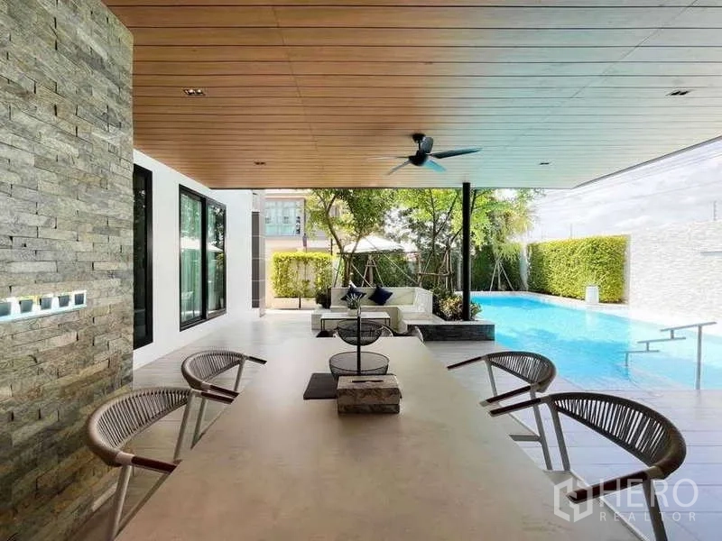 Detached House for sale in Bang Lamung, Chon Buri - Covered outdoor dining area with ceiling fan, stone feature wall and views to the swimming pool.