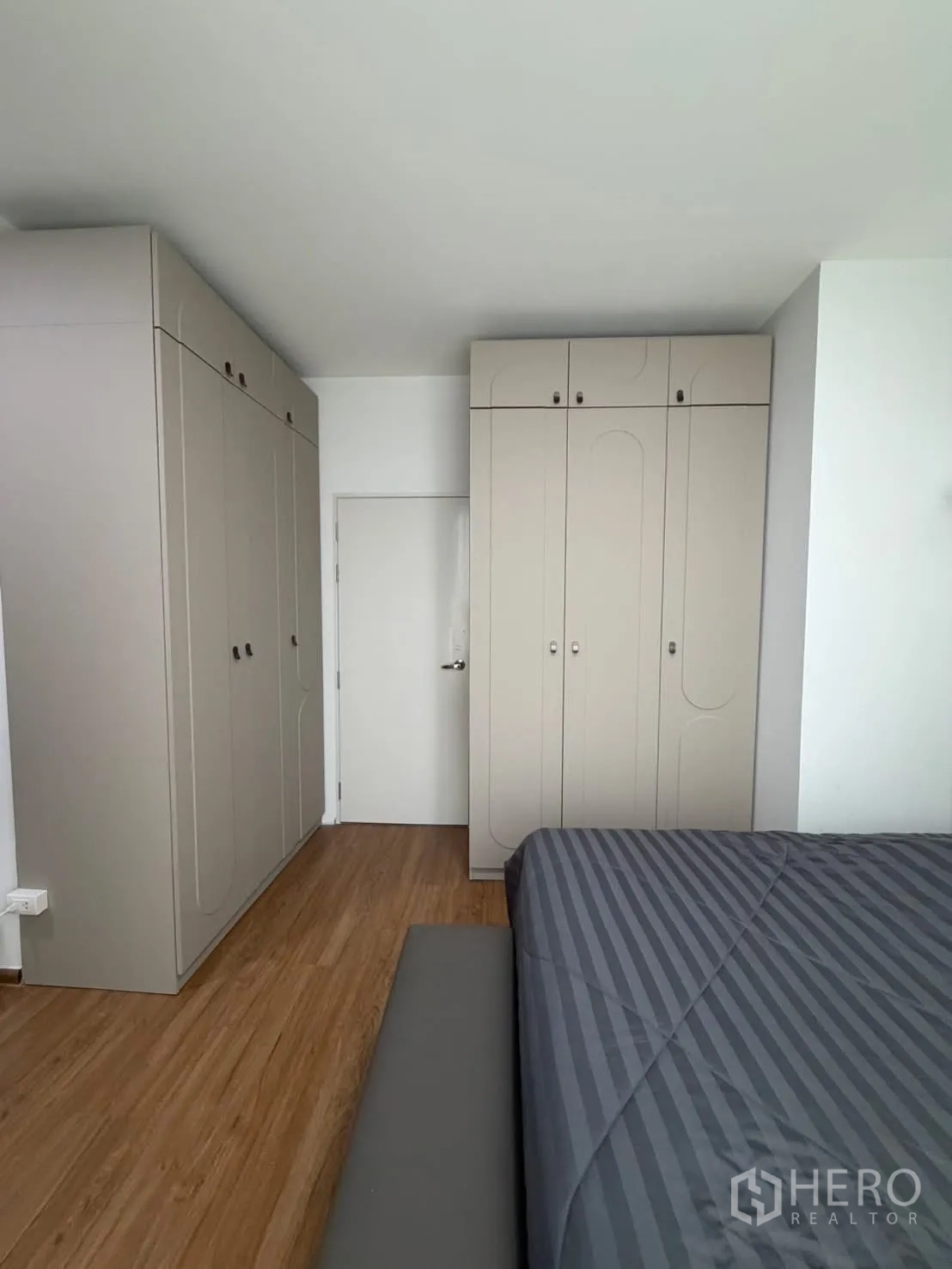 Townhouse for rent in Bang Phli, Samut Prakan - Bedroom with built-in beige wardrobes, wood flooring and part of a double bed visible.