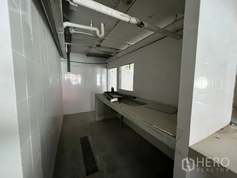 零售空间 出租在Watthana, Bangkok - 瓷砖后厨配操作台与排水沟，顶部可见管道。