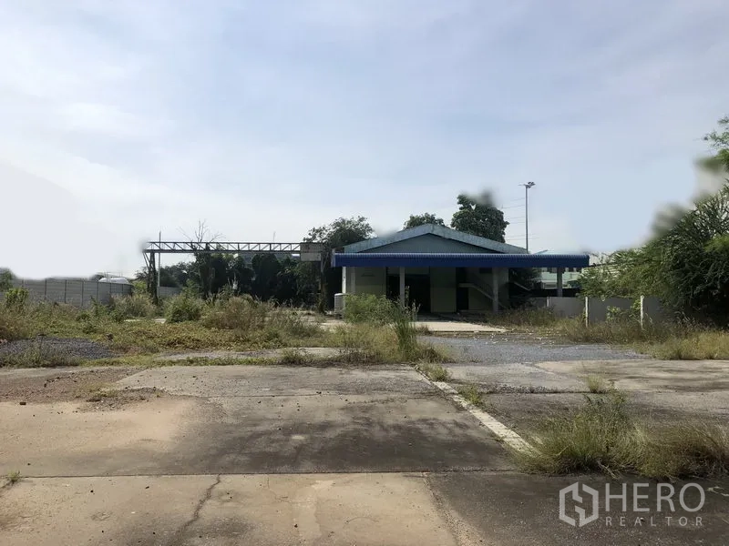货栈 出租或出售在Lam Luk Ka, Pathum Thani - 宽阔的混凝土场地，中央有一栋蓝顶小办公楼，四周杂草丛生。