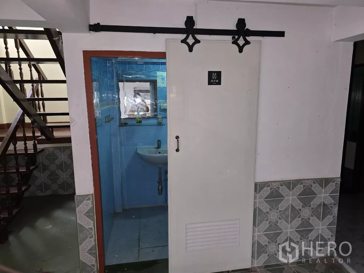 Home Office for rent in Wang Thonglang, Bangkok - Ground-floor bathroom with blue tiles and basin, seen through a sliding door beside the stairs.