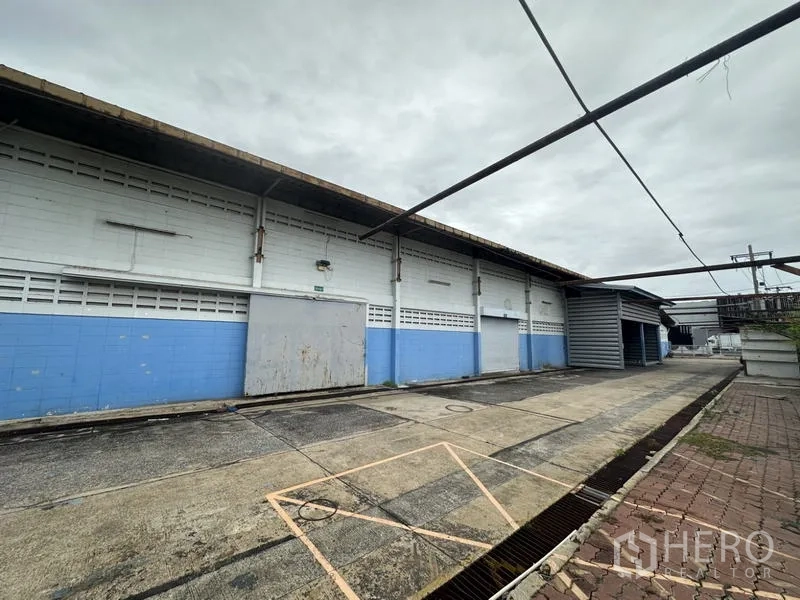โรงงาน ขายในKhlong Luang, Pathum Thani - ผนังภายนอกโกดังยาว พร้อมประตูโหลดและทางเดินบริการมีหลังคา