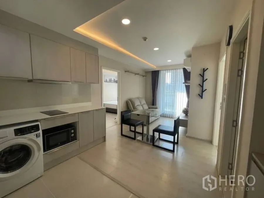 Condominium for rent in Khlong Toei, Bangkok - Open kitchen with washer and microwave beside a bright lounge leading to a balcony.