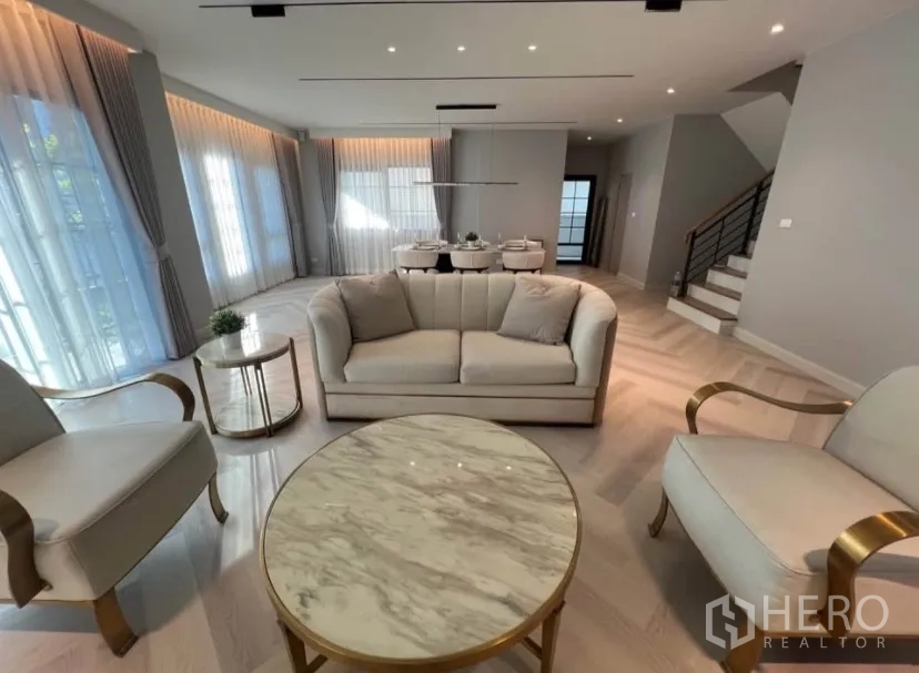 Detached House for rent in Bang Phli, Samut Prakan - Elegant open-plan living room with sofa set, marble coffee table, dining area and staircase, wrapped by full-height curtains.