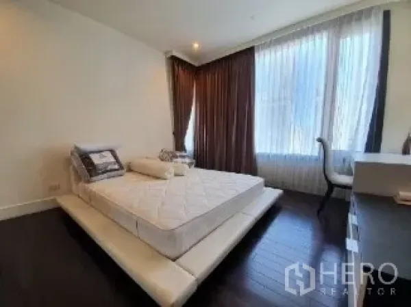 คอนโด ขาย - ห้องนอนหลักเตียงยกพื้น พื้นไม้สีเข้ม และหน้าต่างบานใหญ่พร้อมผ้าม่าน