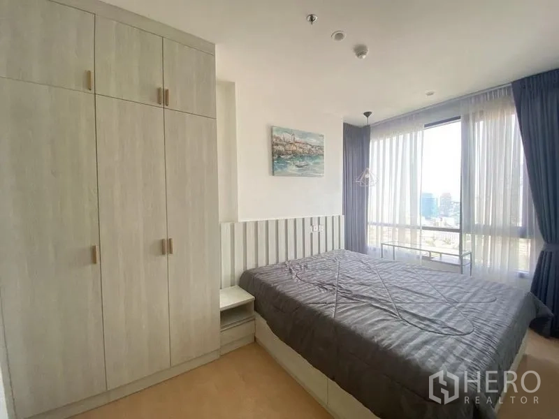Condominium for rent in Watthana, Bangkok - Master bedroom with large wardrobe, king bed, and corner windows with city views and sheer curtains.