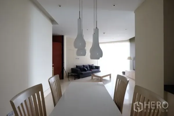 Condominium for rent in Bang Rak, Bangkok - Dining area with modern pendant lights, white table and chairs facing the living room.