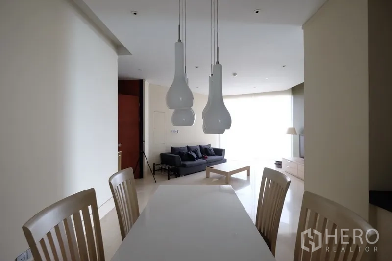 Condominium for rent in Bang Rak, Bangkok - Dining area with modern pendant lights, white table and chairs facing the living room.