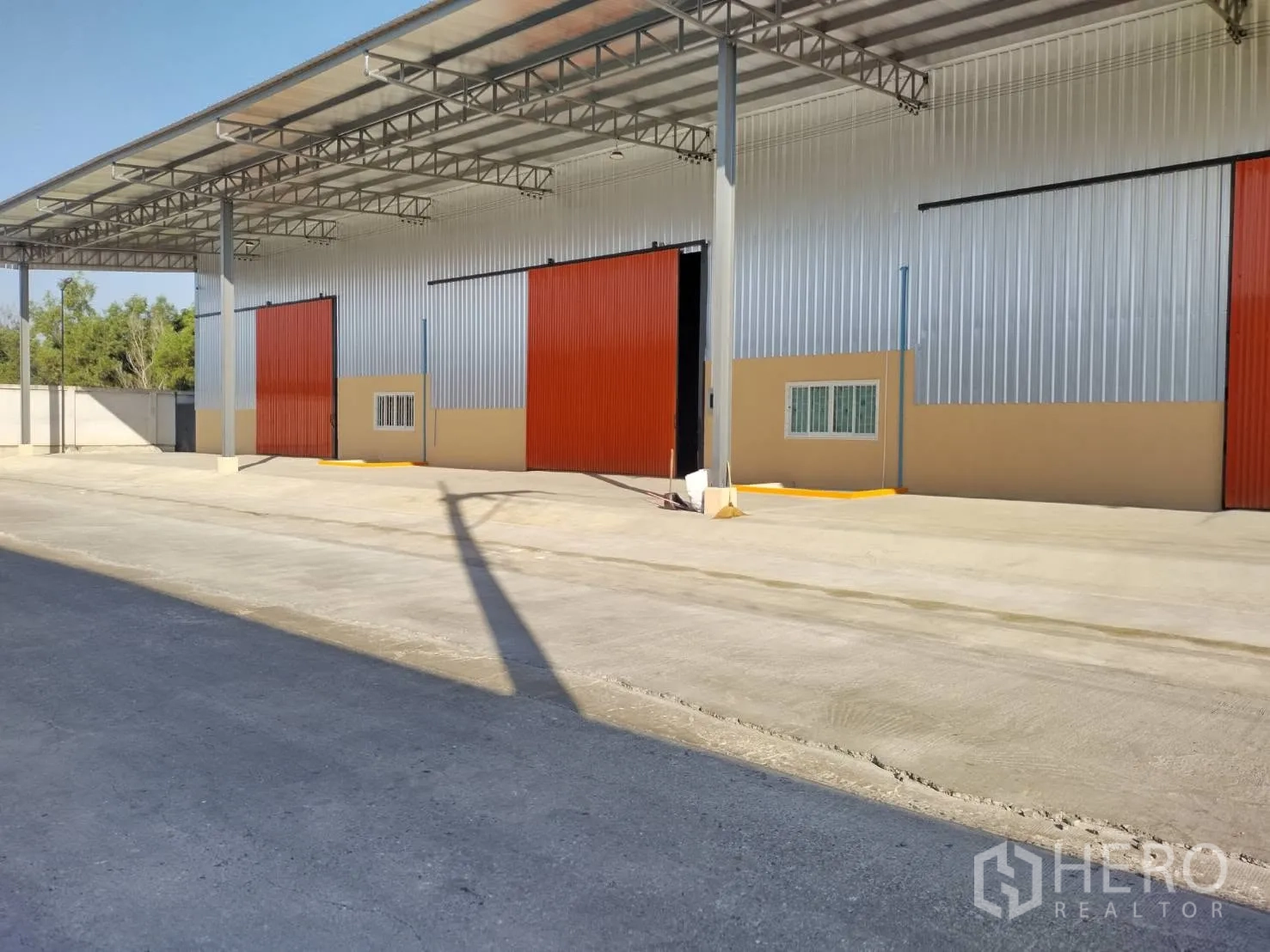 โกดัง for rent in Khlong Luang, Pathum Thani - ด้านหน้าโกดังเปิดประตูบานเลื่อน มีเสาเหล็ก และลานคอนกรีตลึกสำหรับโหลดสินค้า