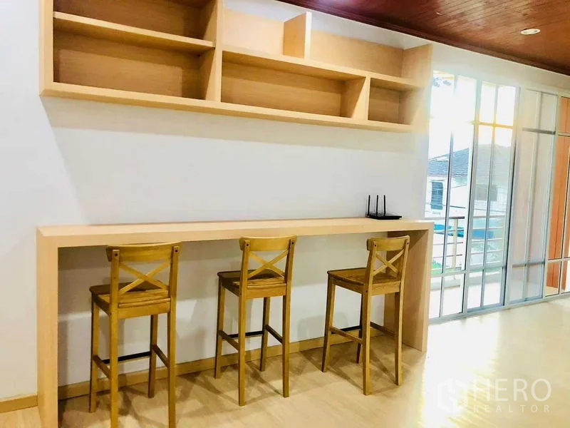 Home Office for rent or sale in Pak Kret, Nonthaburi - Work area with long built-in counter, wooden stools, open shelves and sliding glass doors to a balcony.