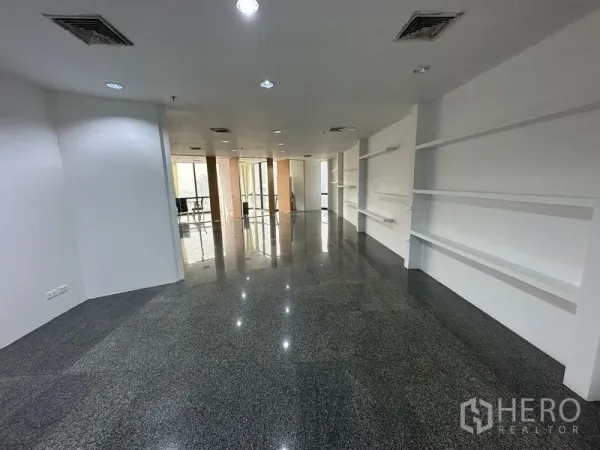 办公空间 出租 - 开放工作区，深色石材地面、嵌入式照明与展示搁架，通往会议室。