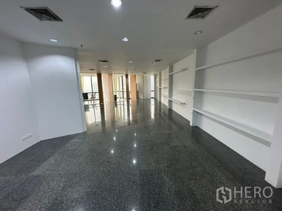 办公空间 出租 - 开放工作区，深色石材地面、嵌入式照明与展示搁架，通往会议室。