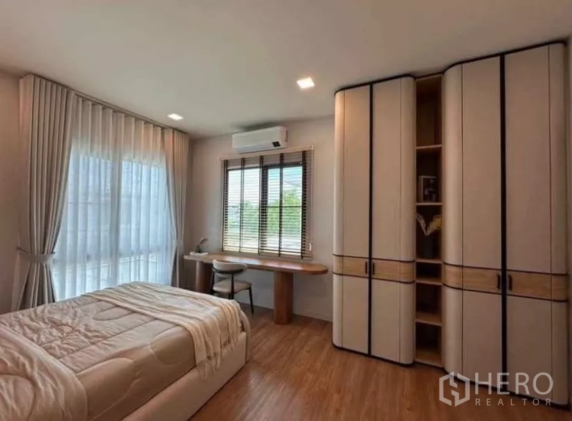 Detached House for rent in Samut Prakan - Bedroom with rounded-edge wardrobes, wood floors, and study desk by windows.